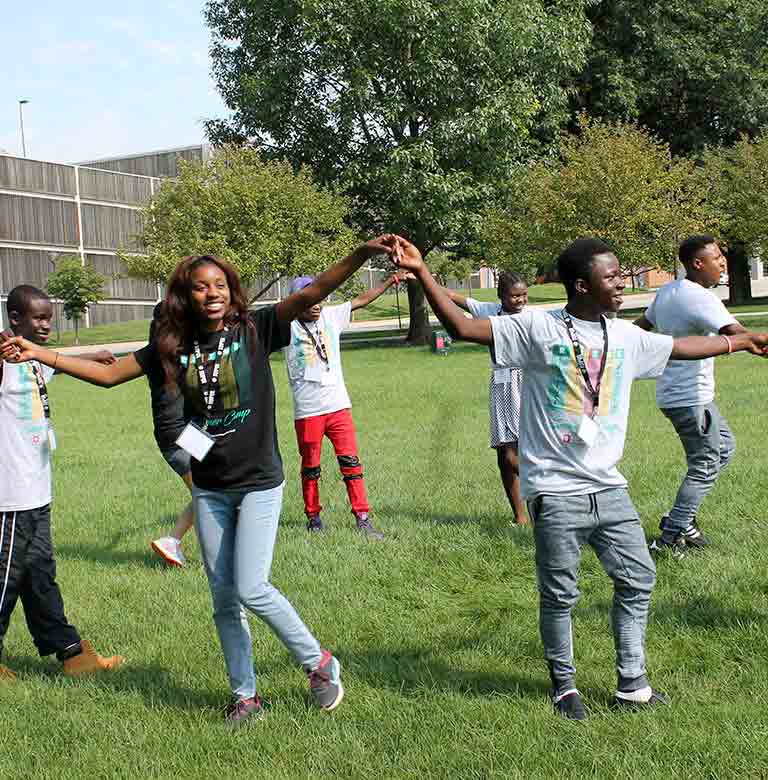 Refugee teenagers stand in a circle outside and hold hands.