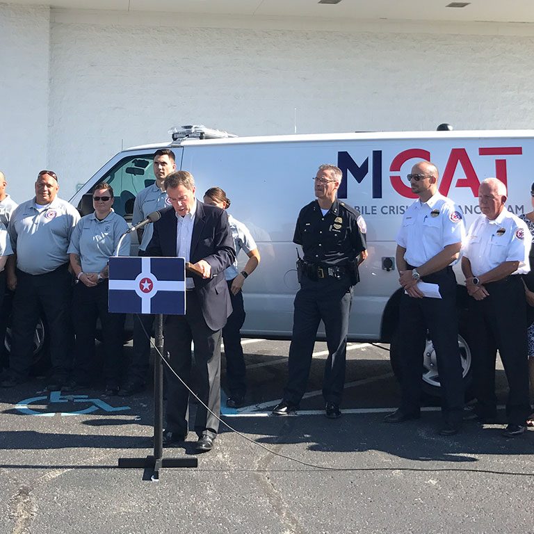 Indianapolis Mayor Joe Hogsett speaks while public safety workers stand by an MCAT van.